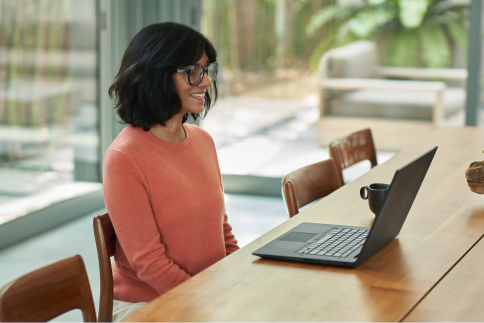 A person smiles at their laptop in an office setting.